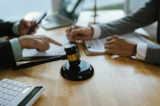Mazo de madera sobre una mesa mientras dos personas revisan documentos